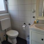 Badezimmer mit Toilette, Waschbecken und Spiegel. Fenster sorgt für Tageslicht.