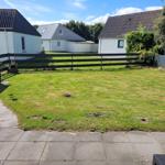 Garten mit Rasenfläche und Terrasse, umgeben von Zaun und Nachbarhäusern.