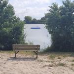 Holzbank am Ufer mit Blick auf einen See und eine schwimmende Plattform.