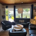 Wohnzimmer mit schwarzen Ledermöbeln, Holzdecke und Blick auf Garten.