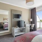 Zimmer mit Bett, Fernseher, Kühlschrank und Balkon mit Blick.