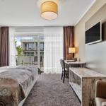 Schlafzimmer mit Bett, Schreibtisch und TV. Balkon mit Sicht auf Gebäude.