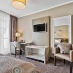 Schlafzimmer mit Bett, Schreibtisch, Fernseher und Sessel.