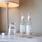 Auf dem Tisch stehen zwei Mineralwasserflaschen und ein Glas neben einer Lampe.