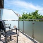 Terrasse mit Stühlen und Tisch, Glasgeländer und Blick auf Bäume.