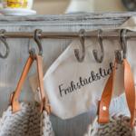 Haken an einer Holzwand mit Beuteln und einem Stoffbeutel mit Aufschrift.