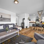 Wohnzimmer mit Sofa, Kamin und Essbereich. Holzboden und Küchenzeile sichtbar.