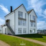 Modernes weißes Haus mit Balkon und Terrasse an Wasser.