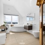 Badezimmer mit Badewanne, Waschmaschine und Toilette. Blick auf Hafen durch Fenster.