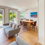 Wohn- und Essbereich mit Sofa, Tisch und Stühlen. Durchgänge zu einem Garten.