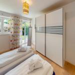 Zwei Betten, Schwebetüren-Schrank und Fenster mit bunten Vorhängen.