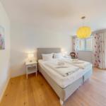 Ein Schlafzimmer mit Doppelbett, Holzboden und Blick auf den Garten.