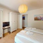 Zimmer mit zwei Betten, weißen Schränken und Holzboden. Hängelampe und Wandbild.