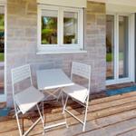 Terrasse mit weißem Tisch und zwei Stühlen vor Steinmauer und Glasfront.