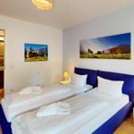 Zwei Betten mit weißen Bettwäsche und Kissen. Wandbilder mit Kühen und Bergen. Holzboden und Nachttische.