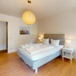 Schlafzimmer mit Bett, Nachttischen und Stuhl auf Holzboden.