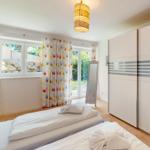 Zwei Betten, Gardinen, Schrank und Fenster mit Blick auf Garten.