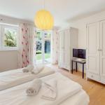 Zwei Betten mit weißen Laken, weiße Schränke, Fenster mit Blick auf Garten.