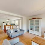 Wohnzimmer mit Sofa, TV und Glasvitrine. Küche im Hintergrund sichtbar.