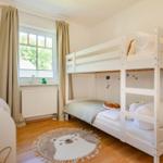 Kinderzimmer mit Doppelstockbett, Fenster, Teppich und Bücherregal.