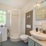 Badezimmer mit Dusche, Waschbecken und Toilette. Fenster mit Blick auf Grün.