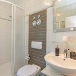 Badezimmer mit Dusche, Waschbecken und Toilette. Fliesen und Spiegel sind sichtbar.