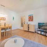 Wohn- und Essbereich mit Holzboden, TV, Tisch und Stühlen sowie Wandbildern.