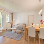 Wohn- und Essbereich mit Sofa, Tisch und Stühlen. Durchgang zur Terrasse mit Blick auf Grün.