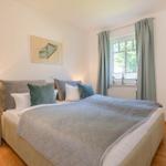 Schlafzimmer mit Bett, Nachttisch und Fenster mit Vorhängen.