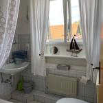 Badezimmer mit Waschbecken, Toilette und Fenster mit Vorhängen.