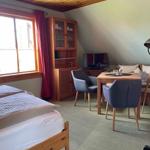 Zimmer mit Bett, Esstisch, TV und Holzmöbel. Fenster mit roten Vorhängen.