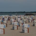 Strand mit Strandkörben, Leuchtturm und Segelyacht im Hintergrund.