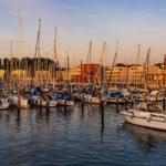 Hafen mit zahlreichen Segelyachten und modernen Gebäuden im Hintergrund.
