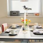 Esstisch mit vier Stühlen, Blumen und Kerzen auf der Fensterbank.