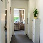 Flur mit weißen Wänden, Pflanze und Blick in Wohnzimmer mit Sofa.