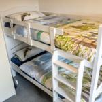 Doppelstockbett mit Matratzen und Bettwäsche. Neben einem Kleiderschrank.