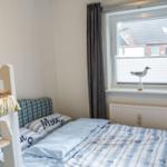 Zimmer mit Doppelbett und Etagenbett, Fenster mit Jalousie und Vogeldekoration.