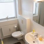 Badezimmer mit Toilette, Waschbecken und Dusche. Fenster mit Jalousie und Heizkörper.