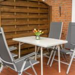 Terrasse mit Tisch und vier Stühlen, Blumen in Vase, Holz- und Ziegelwand