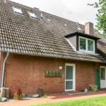 Ein Haus mit Backsteinfassade und Dachgauben. Vorgarten mit Rasen und Pflanzen.