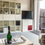 Wohnzimmer mit Bücherregal, TV und Sitzgelegenheit. Draußen liegt ein Wickerstuhl.