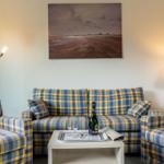 Wohnzimmer mit kariertem Sofa, Tisch mit Champagner und Wandbild.