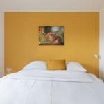 Schlafzimmer mit Bett, gelber Wand und Wandbild mit Eichhörnchen.