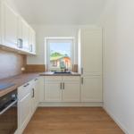 Küche mit weißen Schränken, Holzoberflächen und Fensterblick.