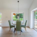 Esszimmer mit runden Tisch, grünen Stühlen und großen Fenstern zur Aussicht.