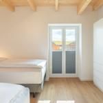 Schlafzimmer mit zwei Betten, Holzboden und Balkontür.