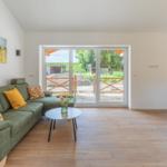 Grünes Sofa mit Kissen, Holzboden und Glastüren zur Terrasse.