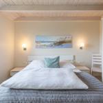 Schlafzimmer mit Bett, Nachttischen und Wandbild. Holzdecke und Fenster.