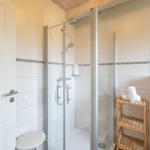 Dusche mit Glaswand, Holzregal und weißen Fliesen.