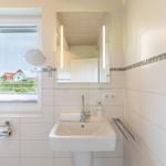 Badezimmer mit Waschbecken, Spiegel und Fensterblick auf Haus und Garten.